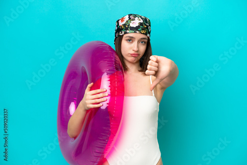 Young Ukrainian woman holding air mattress isolated on blue background showing thumb down with negative expression