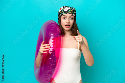 Young Ukrainian woman holding air mattress isolated on blue background surprised and pointing front