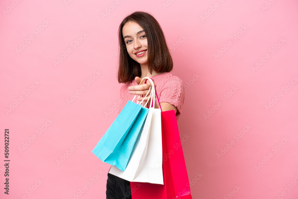 Young Ukrainian woman isolated on pink background holding shopping bags and giving them to someone