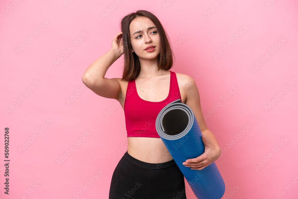 Young sport Ukrainian woman going to yoga classes while holding a mat isolated on pink background having doubts Young sport Ukrainian woman going to yoga classes while holding a mat isolated on pink background having doubts
