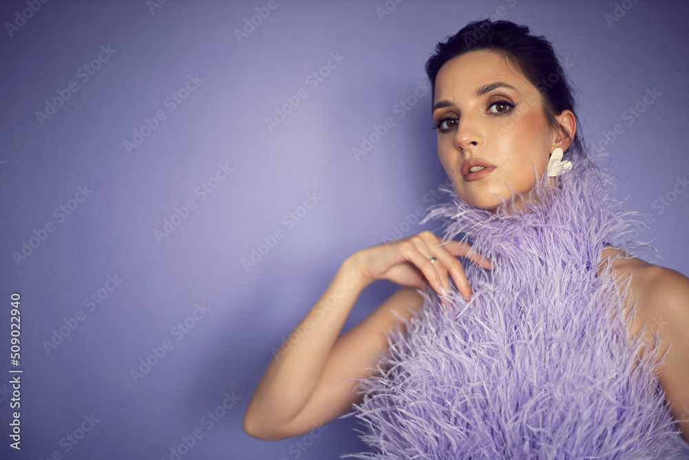 portrait woman in an evening purple dress with feathers stands in the background in the studio.
