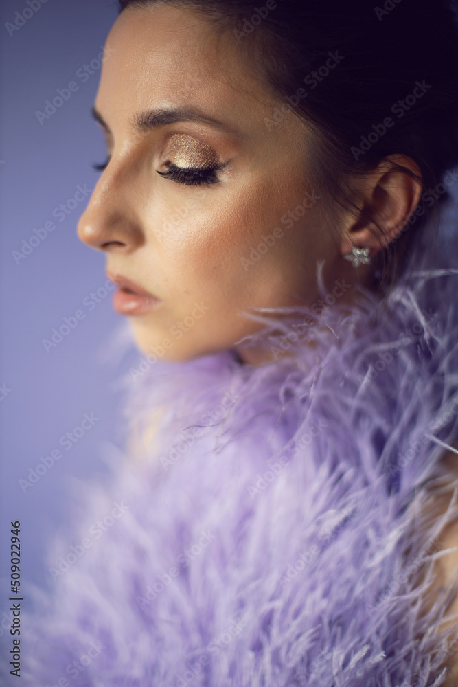 portrait woman in an evening purple dress with feathers stands in the background in the studio. portrait woman in an evening purple dress with feathers stands in the background in the studio.