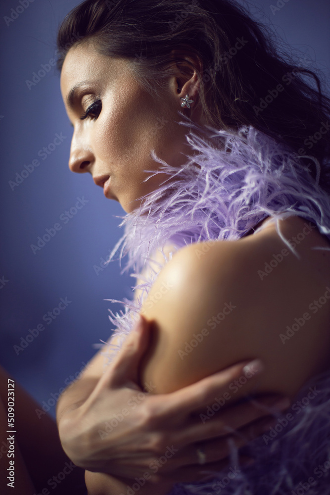 portrait woman in an evening purple dress with feathers stands in the background in the studio.