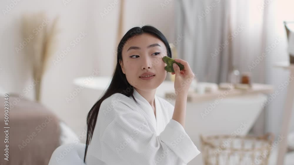 Domestic face sculpting, Young beautiful asian woman making skin lifting massage with green gouache stone, free space Domestic face sculpting, Young beautiful asian woman making skin lifting massage with green gouache stone, free space