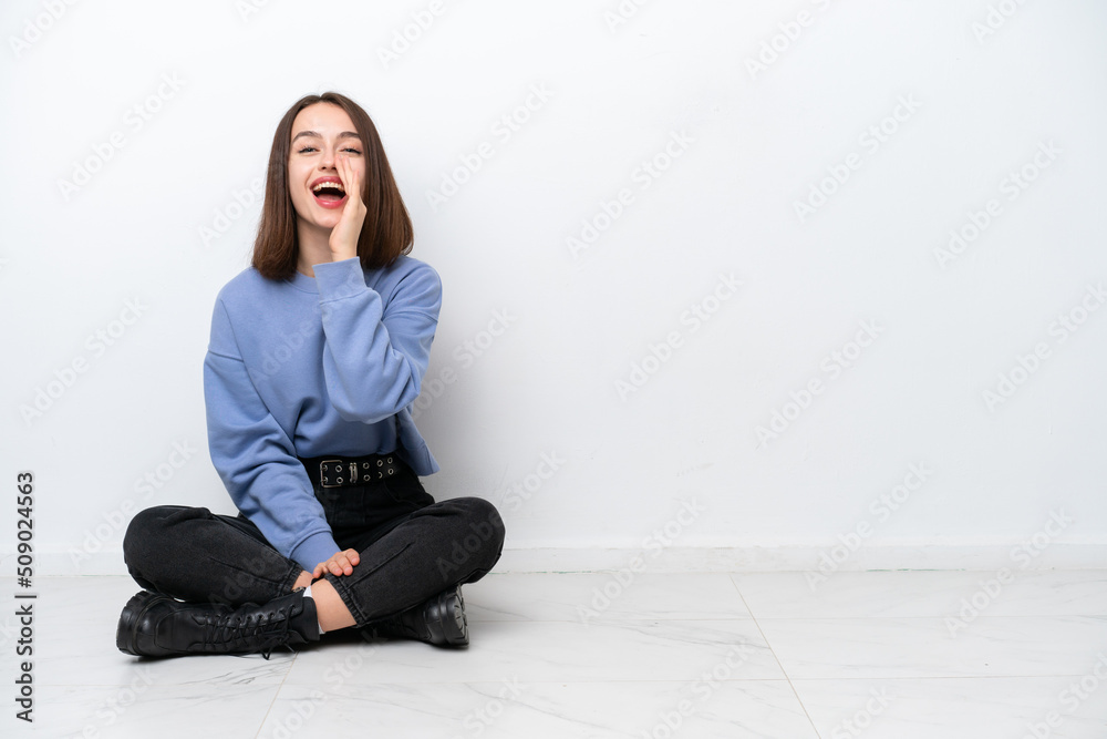 Young Ukrainian woman sitting on the floor isolated on white background shouting with mouth wide open