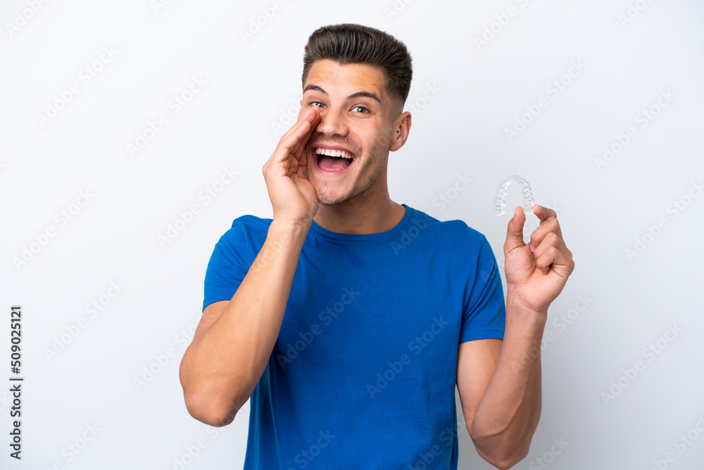 Young caucasian man holding invisible braces isolated on white background shouting with mouth wide open Young caucasian man holding invisible braces isolated on white background shouting with mouth wide open