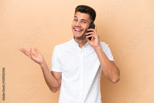 Young caucasian man isolated on beige background keeping a conversation with the mobile phone with someone