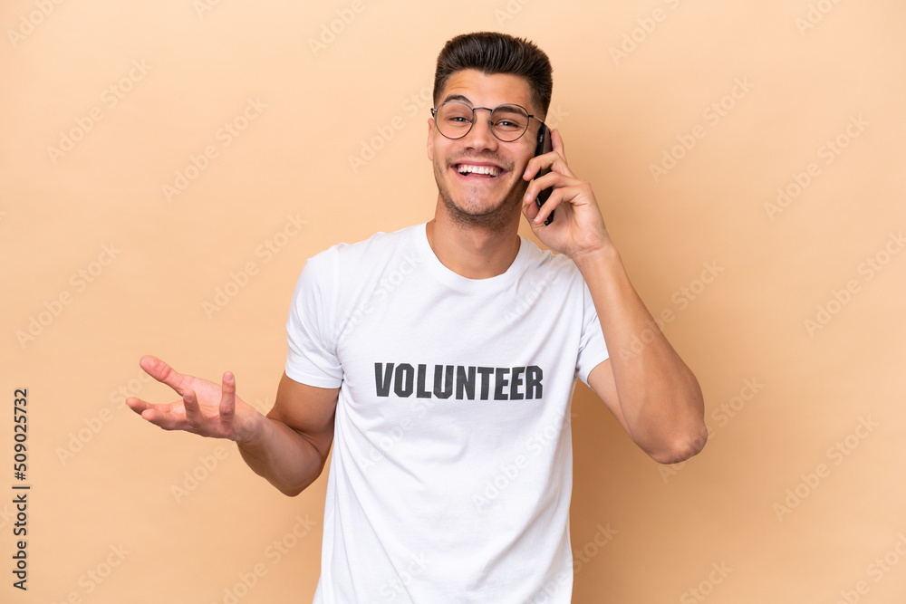 Fototapeta premium Young volunteer caucasian man isolated on beige background keeping a conversation with the mobile phone with someone