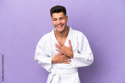 Young caucasian man doing karate isolated on purple background smiling a lot