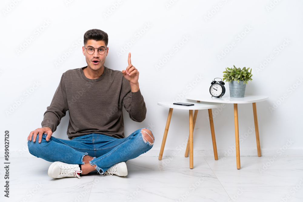 Young caucasian man sitting in his home isolated on white background intending to realizes the solution while lifting a finger up
