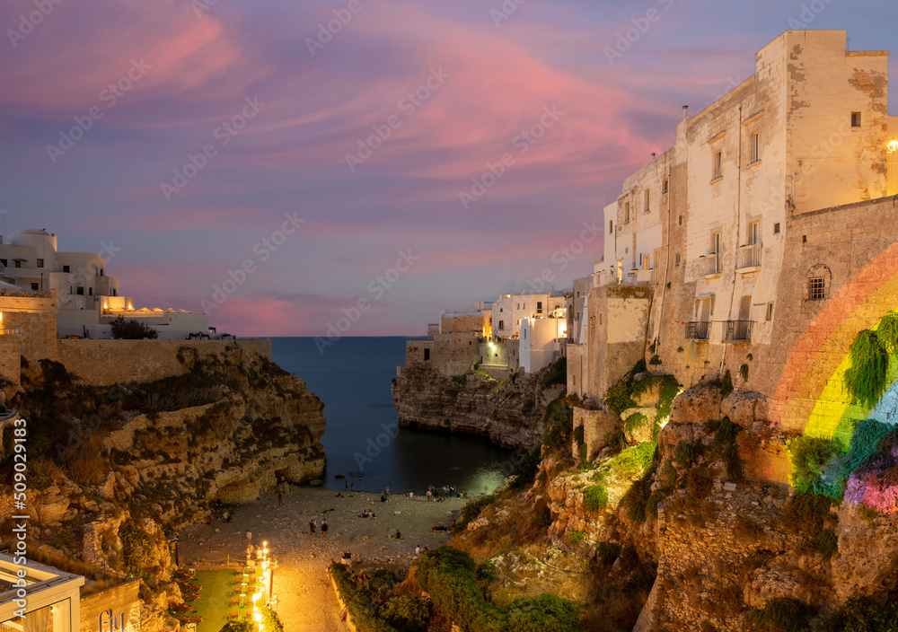 Polignano a mare, Puglia, Italy. August 2021. Incredible aerial view of Cala Monachile: the picturesque and fascinating beach of the historic center. Evening, blue hour.