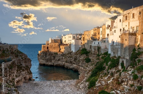 Polignano a mare, Puglia, Italy. August 2021. Amazing aerial view of Cala Monachile: the picturesque and fascinating beach of the historic center. At sunset, the golden hour, people enjoy the place.