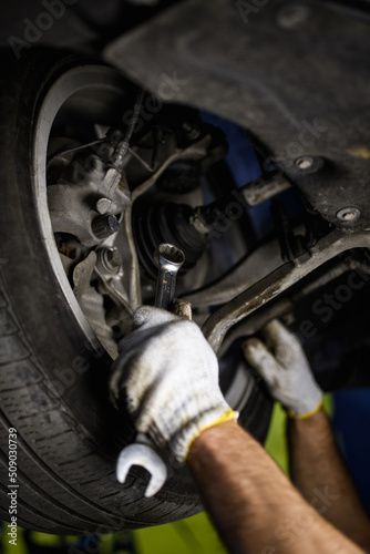 Partial view of mechanic in gloves holding wrench near car wheel in service station 