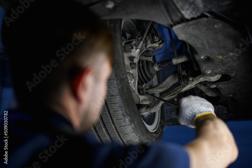 Blurred auto mechanic holding screwdriver near car wheel in garage 