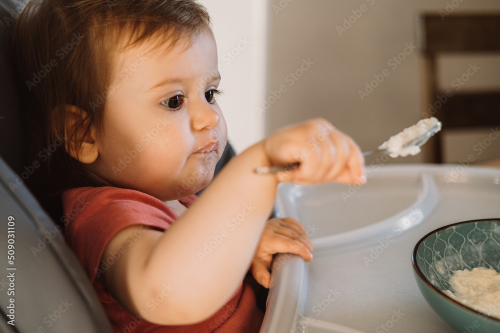 Baby try eating the oatmeal with a spoon from a bowl. Little boy learning to feed herself. Smiling happy child. Baby try eating the oatmeal with a spoon from a bowl. Little boy learning to feed herself. Smiling happy child.