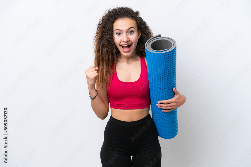 Young sport Arab woman going to yoga classes while holding a mat isolated on white background celebrating a victory in winner position Young sport Arab woman going to yoga classes while holding a mat isolated on white background celebrating a victory in winner position