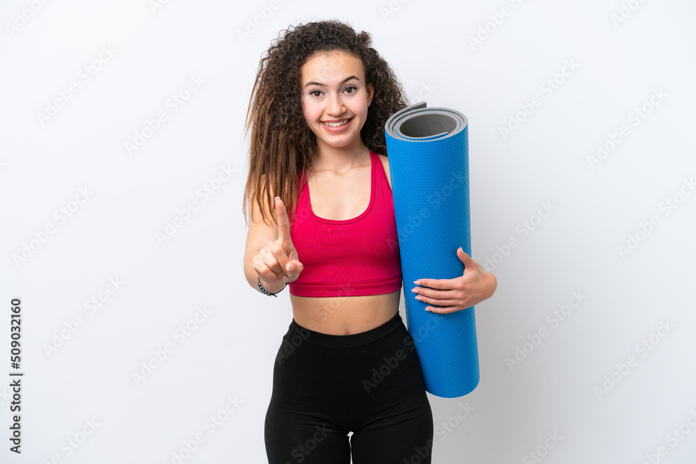 Young sport Arab woman going to yoga classes while holding a mat isolated on white background showing and lifting a finger Young sport Arab woman going to yoga classes while holding a mat isolated on white background showing and lifting a finger
