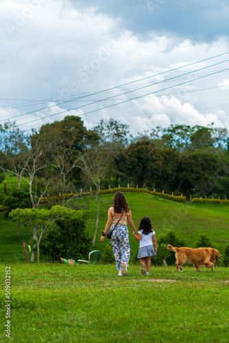 woman walking hand in hand with a little girl or daughter through the field or casual garden with the pet a golden retriever