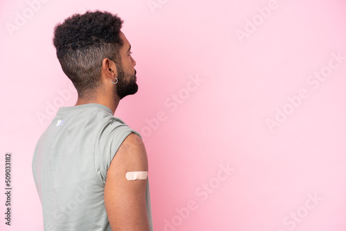 Young Brazilian man wearing a band aid isolated on pink background in back position