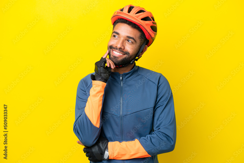 Young cyclist Brazilian man isolated on yellow background thinking an idea while looking up Young cyclist Brazilian man isolated on yellow background thinking an idea while looking up