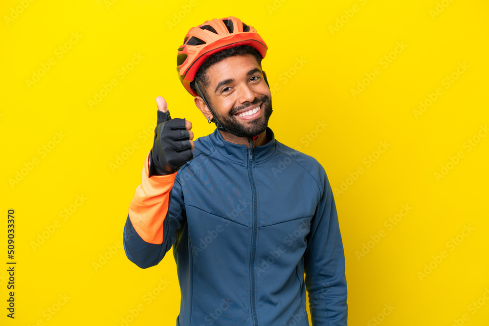 Young cyclist Brazilian man isolated on yellow background with thumbs up because something good has happened