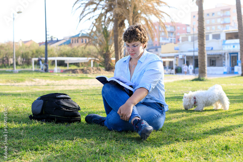 young, overweight woman reading a book on the grass on a sunny day with an urban backdrop