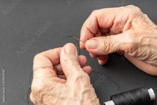 Close up of elderly woman hands pulling thread into the needle.