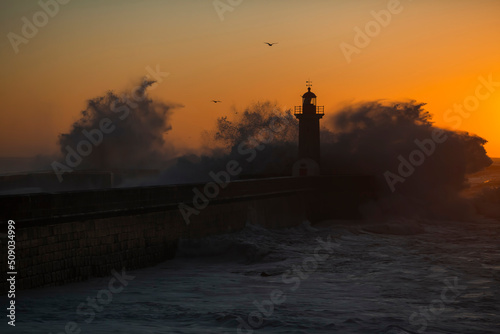 View of the Lighthouse with huge wave during amazing sunset at Atlantic ocean, Porto, Portugal.