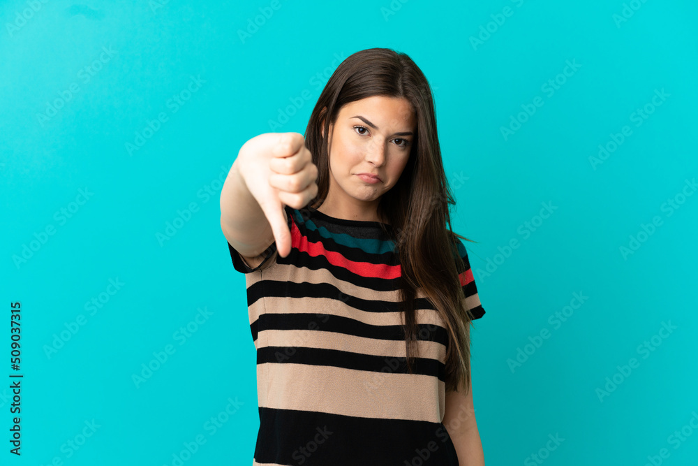 Teenager Brazilian girl over isolated blue background showing thumb down with negative expression Teenager Brazilian girl over isolated blue background showing thumb down with negative expression