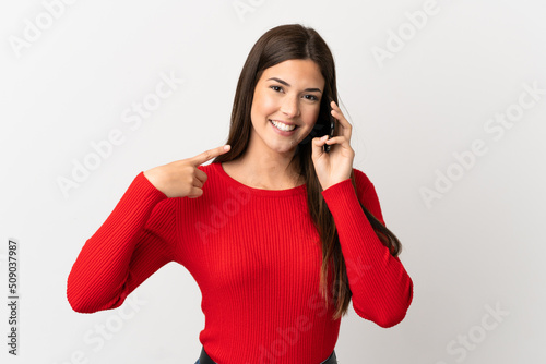 Teenager Brazilian girl using mobile phone over isolated white background giving a thumbs up gesture
