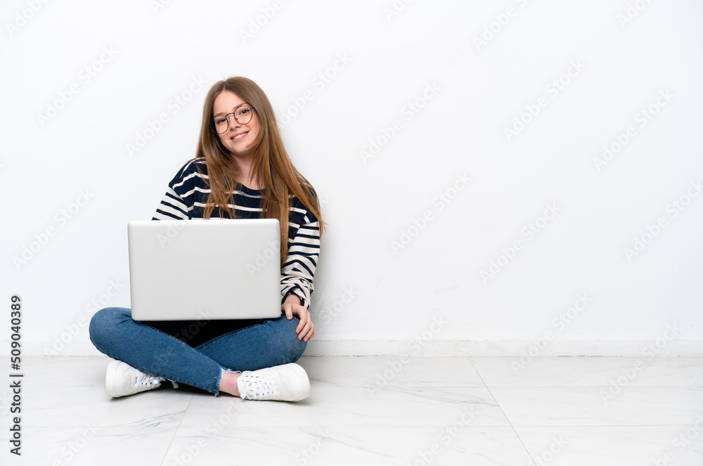 Young caucasian woman with a laptop sitting on the floor isolated on white background with glasses and smiling Young caucasian woman with a laptop sitting on the floor isolated on white background with glasses and smiling