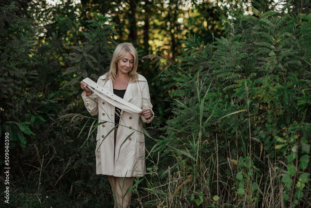 Naklejka premium A beautiful adult woman with blond hair and a light raincoat smiles