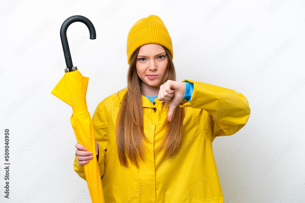 Young caucasian woman with rainproof coat and umbrella isolated on white background showing thumb down with negative expression Young caucasian woman with rainproof coat and umbrella isolated on white background showing thumb down with negative expression