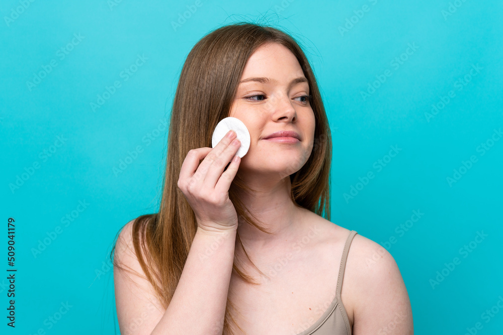 Young caucasian woman isolated on blue background with cotton pad for removing makeup from her face Young caucasian woman isolated on blue background with cotton pad for removing makeup from her face