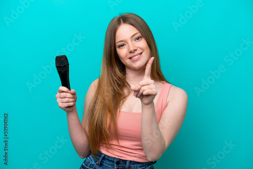 Singer caucasian woman picking up a microphone isolated on blue background showing and lifting a finger