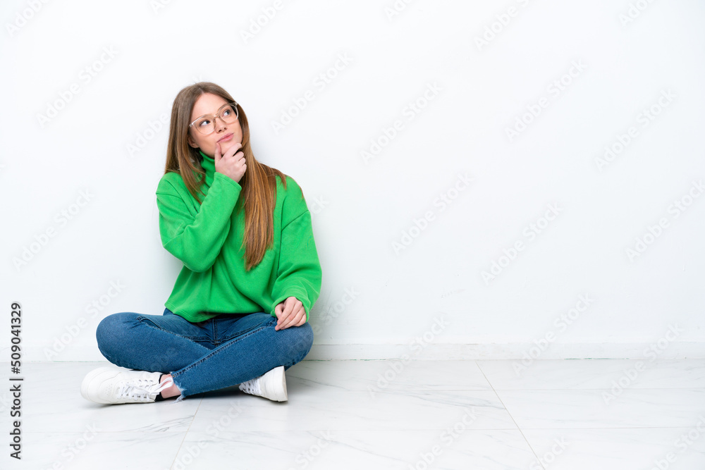 Young caucasian woman sitting on the floor isolated on white background having doubts and with confuse face expression Young caucasian woman sitting on the floor isolated on white background having doubts and with confuse face expression