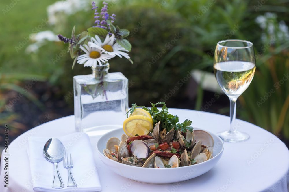 A clam and pasta dish with wine in outdoor setting
