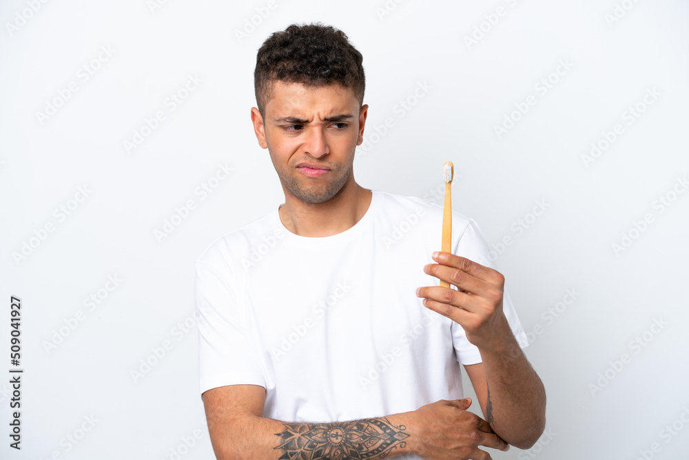 Young Brazilian man brushing teeth isolated on white background with sad expression Young Brazilian man brushing teeth isolated on white background with sad expression