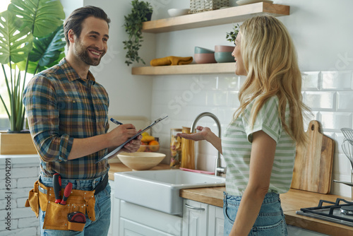 Beautiful young woman talking to male plumber while standing at the kitchen