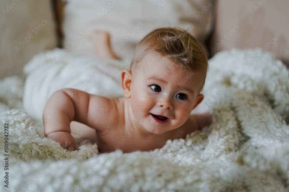 adorable naked 6 month old baby boy lying on belly and looking up in prone position after bathing wrapped in white towel at home on the couch in the living room adorable naked 6 month old baby boy lying on belly and looking up in prone position after bathing wrapped in white towel at home on the couch in the living room