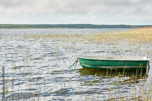 Small green boat anchored in forest lake. Scandinavia. Transportation, traditional craft, recreation, leisure activity, healthy lifestyle, local tourism, sport, rowing, hiking, summer vacations themes photo