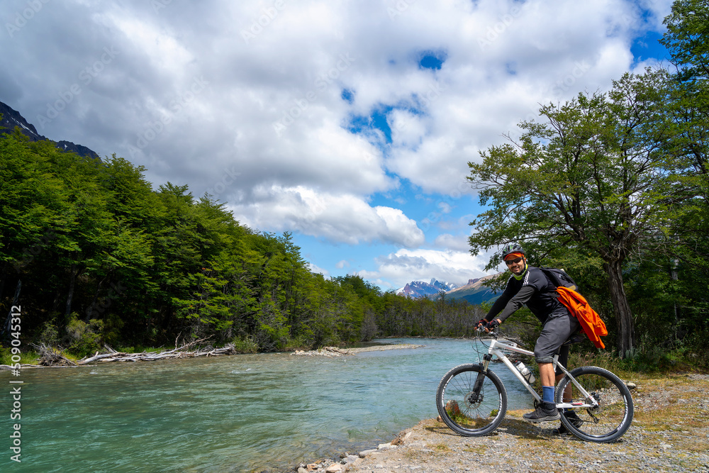 Fototapeta premium man on the bike in the forest next to the river with mountains in the background