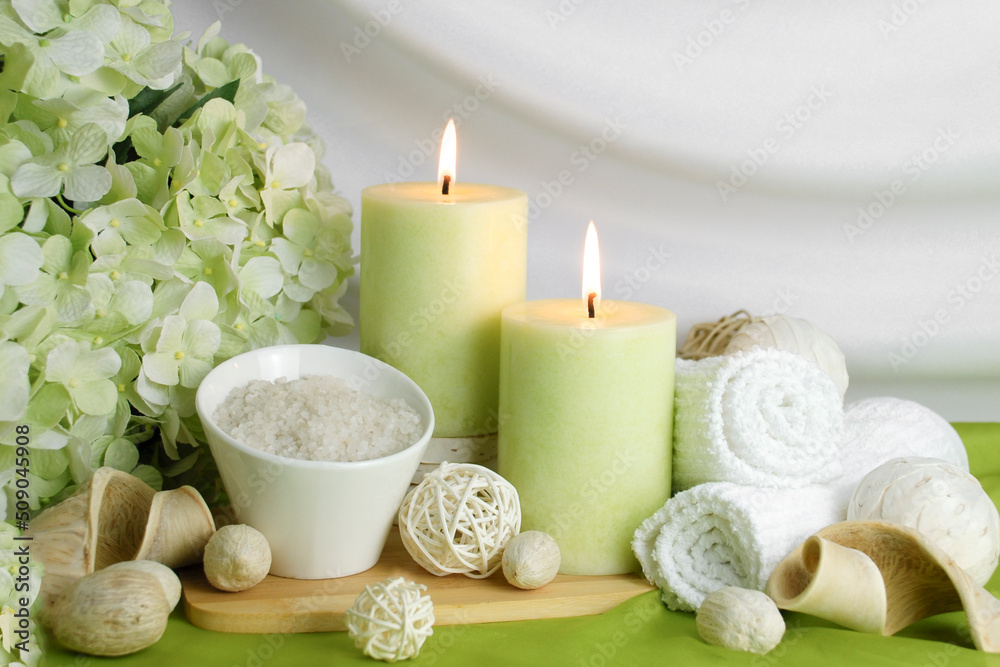 spa concept of soft green orchid flower with burning candles surrounded in natural dried elements, white towels, bath salts against a white elegant swooped background. Spa still life spa concept of soft green orchid flower with burning candles surrounded in natural dried elements, white towels, bath salts against a white elegant swooped background. Spa still life