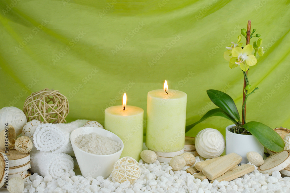 spa concept of soft green orchid flower with burning candles surrounded in natural dried elements, white towels, bath salts against an elegant green swooped backdrop. spa concept of soft green orchid flower with burning candles surrounded in natural dried elements, white towels, bath salts against an elegant green swooped backdrop.
