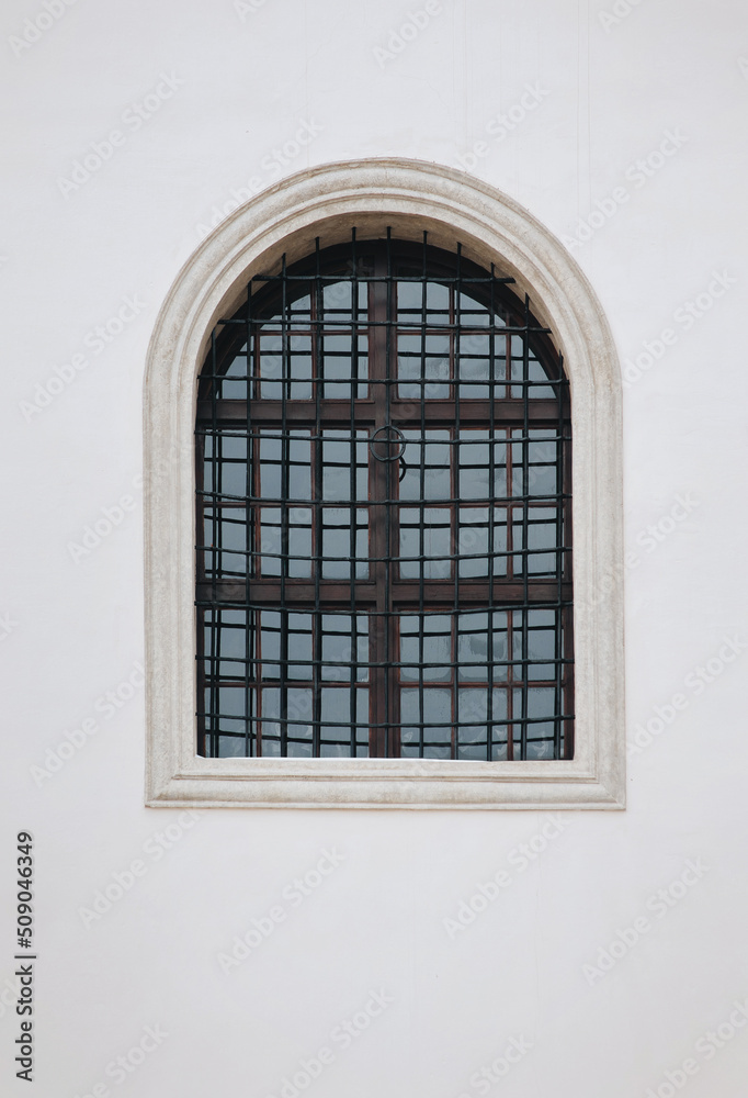 Antique old window with black iron bars framed on a light gray wall. The Jesuit Church in Lviv.