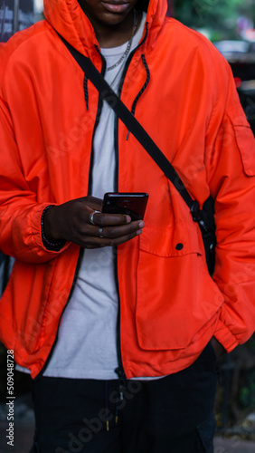 Unrecognizable person texting with his cell phone while wearing a red jacket.