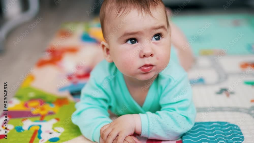 Lovely baby lies on belly looking up. Focused child sticks out his tongue sweetly. Close up. Blurred backdrop. Lovely baby lies on belly looking up. Focused child sticks out his tongue sweetly. Close up. Blurred backdrop.