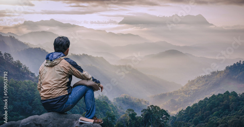 Photo Young male sitting on top of cliff in summer mountains enjoying Sunset or Sunrise Colorful Sky