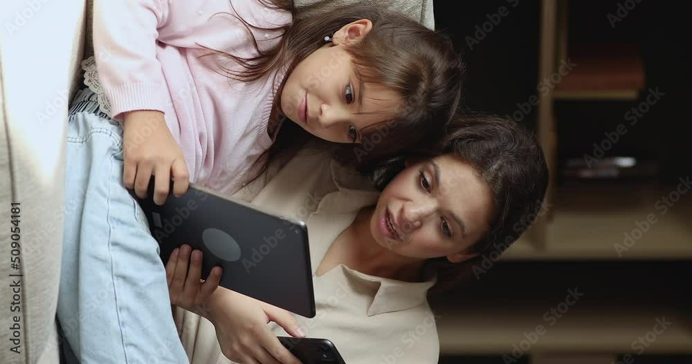 Vertical view mom hold cellphone, little daughter use digital tablet spend time at home with diverse gadgets, have fun, discuss new mobile app. Young gen and modern devices overuse, tech users concept Vertical view mom hold cellphone, little daughter use digital tablet spend time at home with diverse gadgets, have fun, discuss new mobile app. Young gen and modern devices overuse, tech users concept
