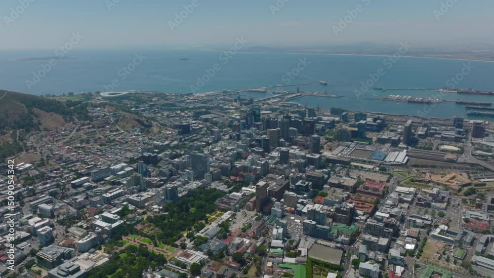 Backwards fly above town. Aerial wide panoramic shot of downtown and surrounding boroughs, sea bay in background. Cape Town, South Africa